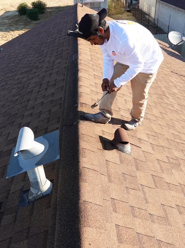 A man standing on top of a roof fixing the shingles.